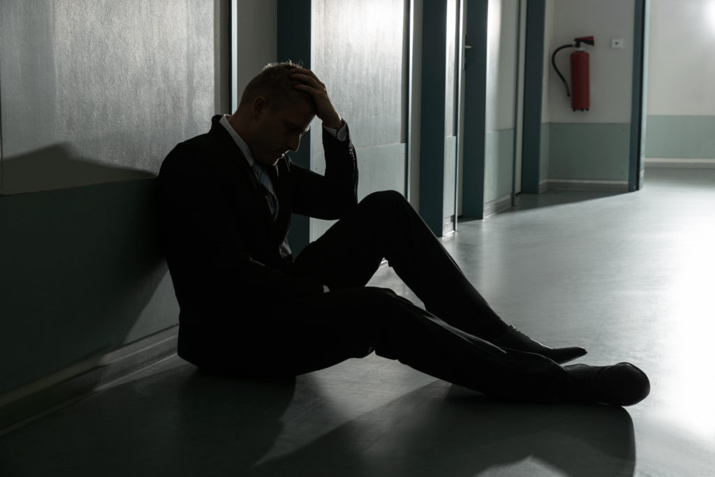 Portrait Of Unhappy Businessman Sitting On Floor In Office Holding His Head
