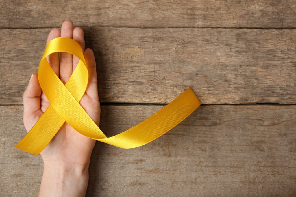 Yellow awareness ribbon in female hand on wooden background.