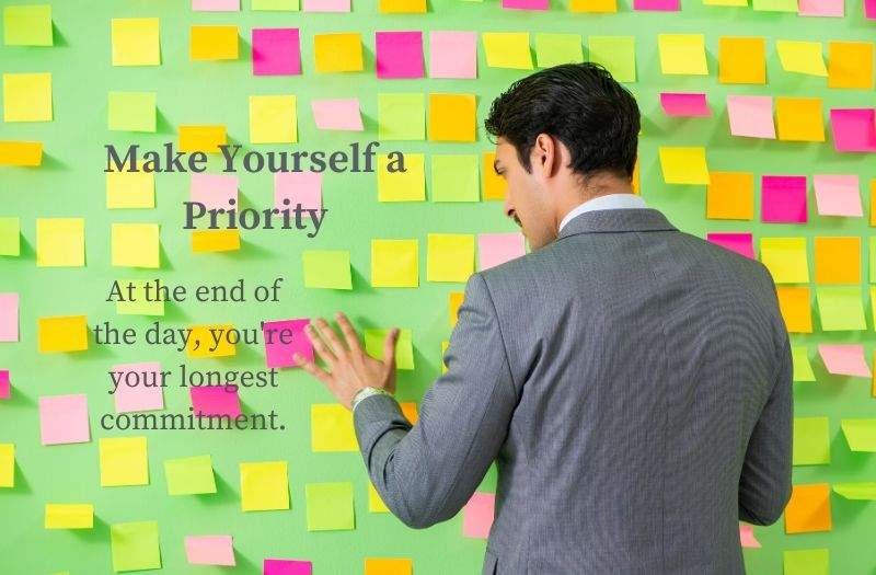 A Man in Front of a Wall of Post It Notes with the Quote - Make Yourself a Priority