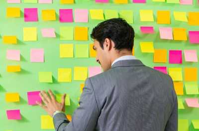 A Man with Many Priorities in Front of a Wall of Post It Notes-Thumbnail